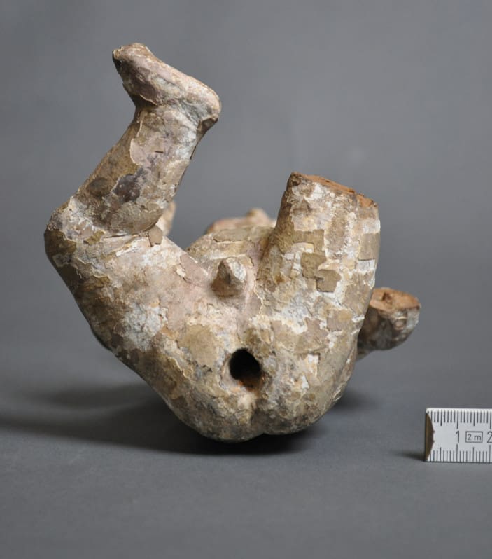 Photograph of a sculpture of a baby showing the underside of the body and the hole for mounting the sculpture on a spike to attach it to another sculpture.